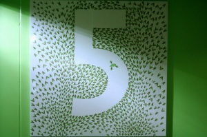 The number 5 on a green background, formed by the absence on the caroony grasshoppers that surround the 5.